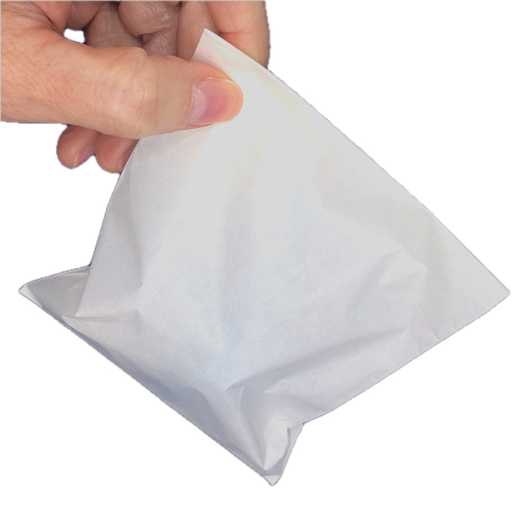 Hand holding a white disposable glassine bag by the corner. The bag is loaded with a resistance spring inside.