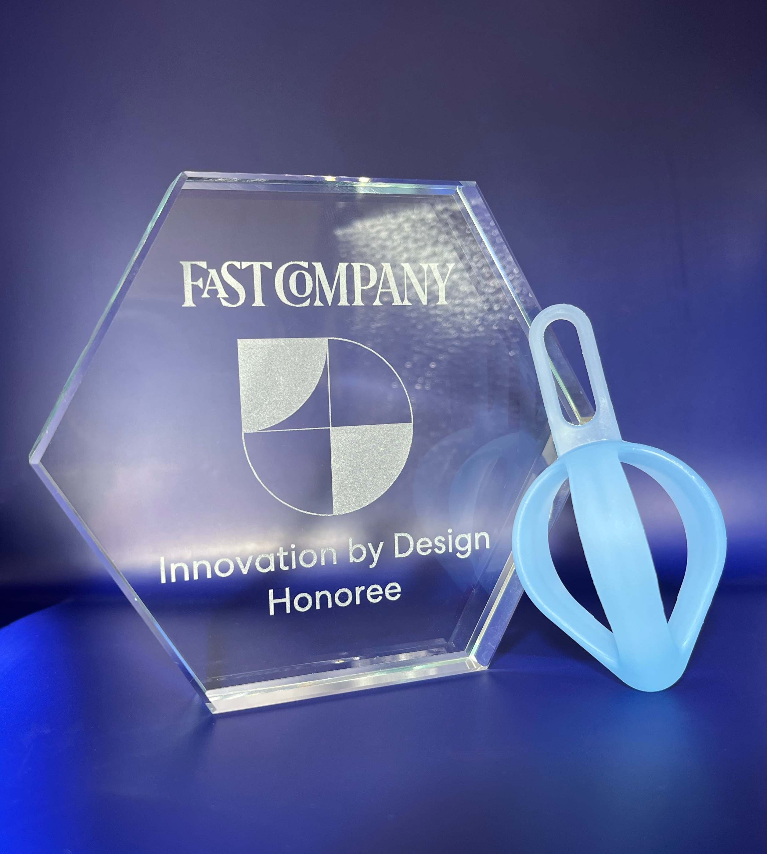 Pippa resistance spring leaning on a hexagonal glass award etched with "Fast Company" wordmark and "Innovation by Design Honoree"
