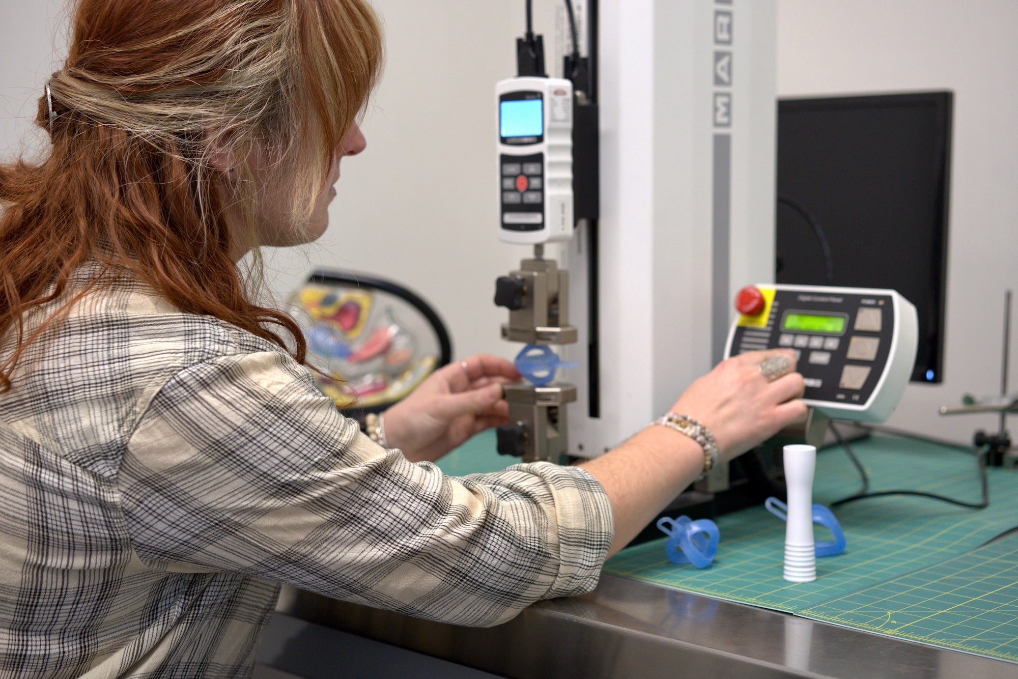 Female engineer using a machine to measure resistance spring force in a workshop setting.
