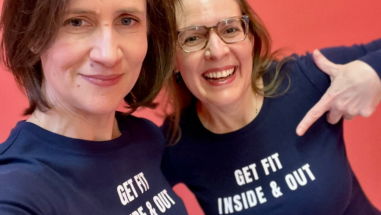 Selfie of Carly and Melody wearing navy blue shirts that read "Get fit inside & out" WHILE standing against a red background
