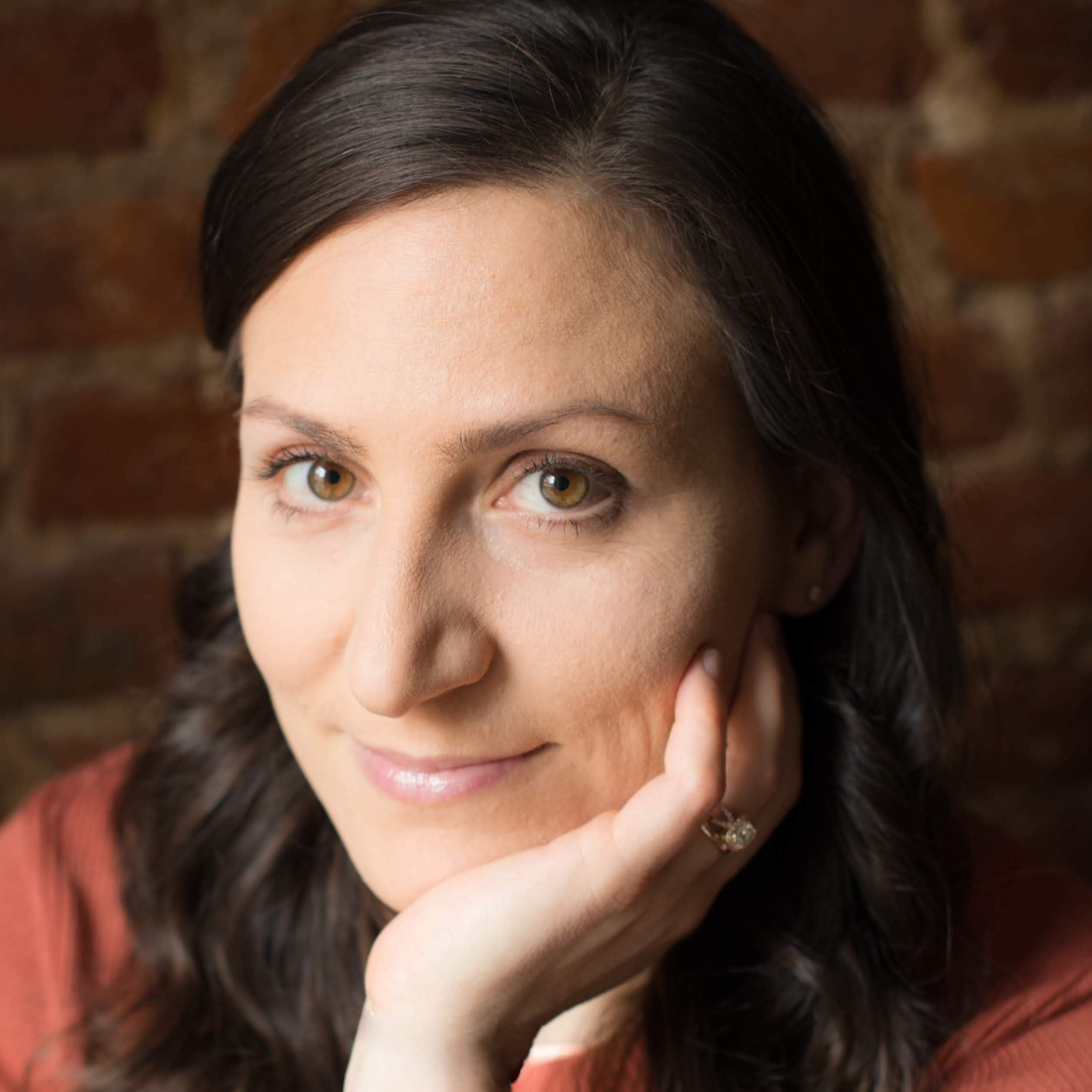 Headshot of Melissa Stendahl, PT, DPT in a terracotta sweater posing with a soft smile against a brick wall.