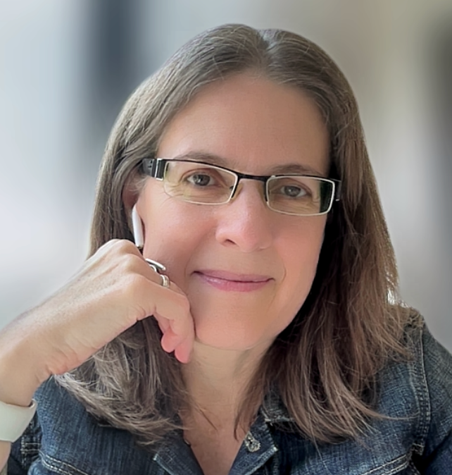 Headshot of Melody Roberts wearing glasses and a denim jacket posing with a soft smile against a blurred background.