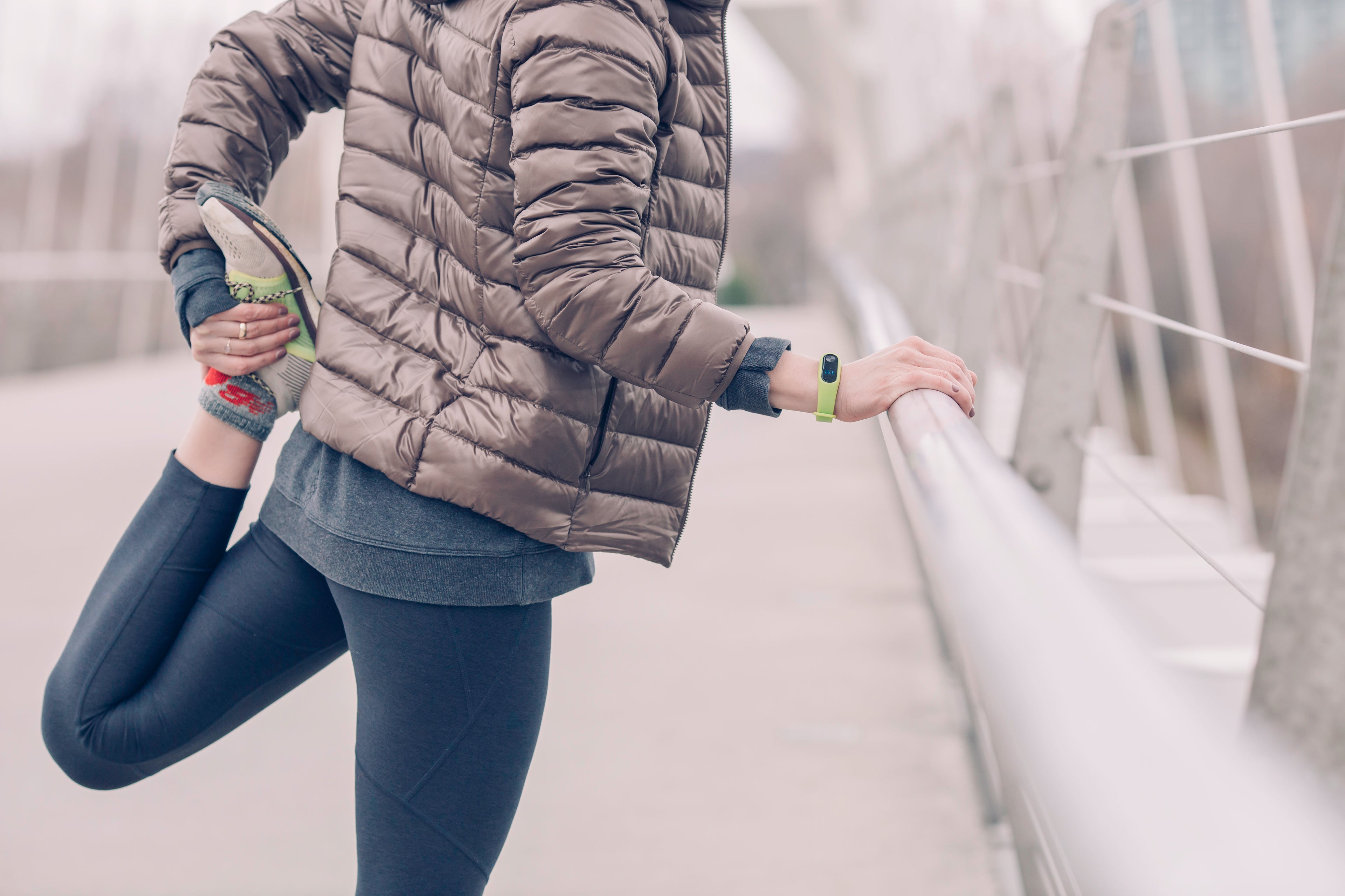 Tightly cropped image of a woman in a puffer coat stretching her left quadracep apparently prior to a run.